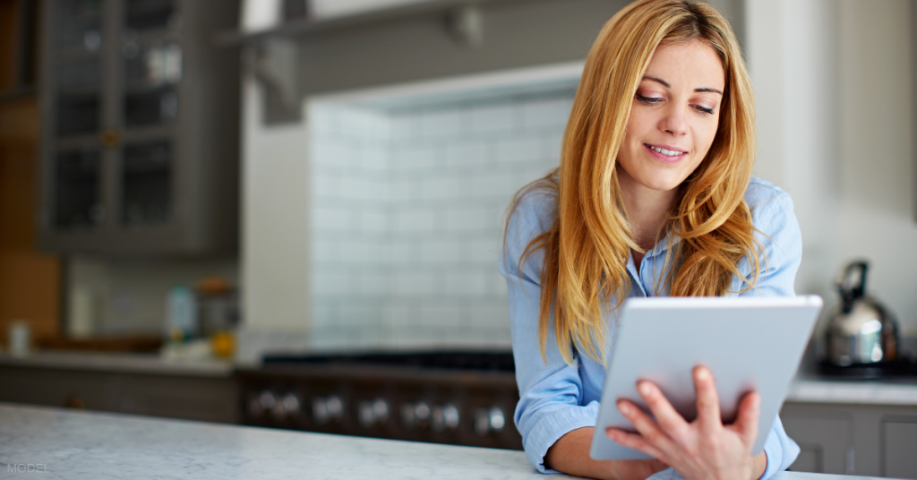 A woman researches the best time of year for plastic surgery on her tablet.