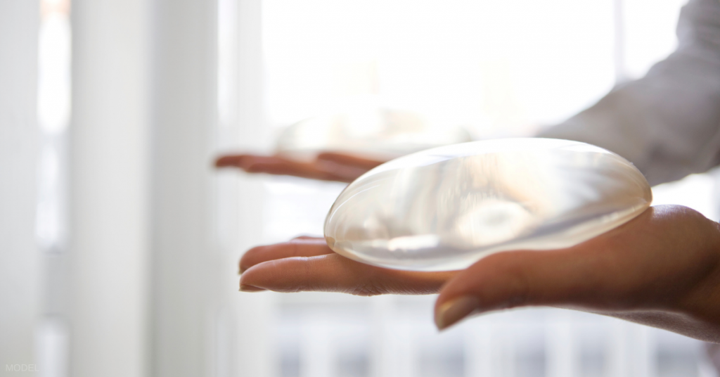 A woman holds saline and silicone implant options in her hands.