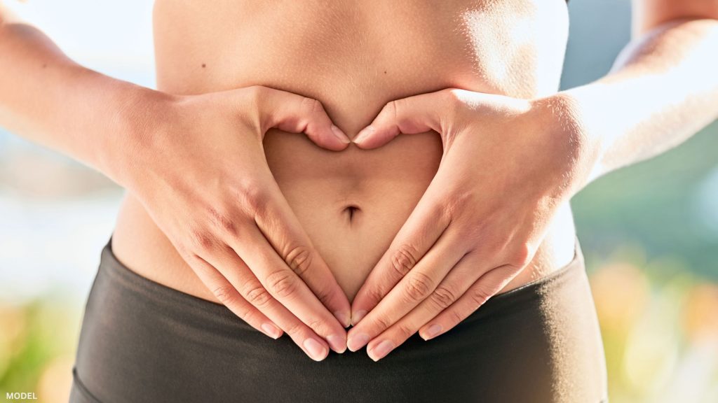Woman forming hand shaped heart around belly button (model)